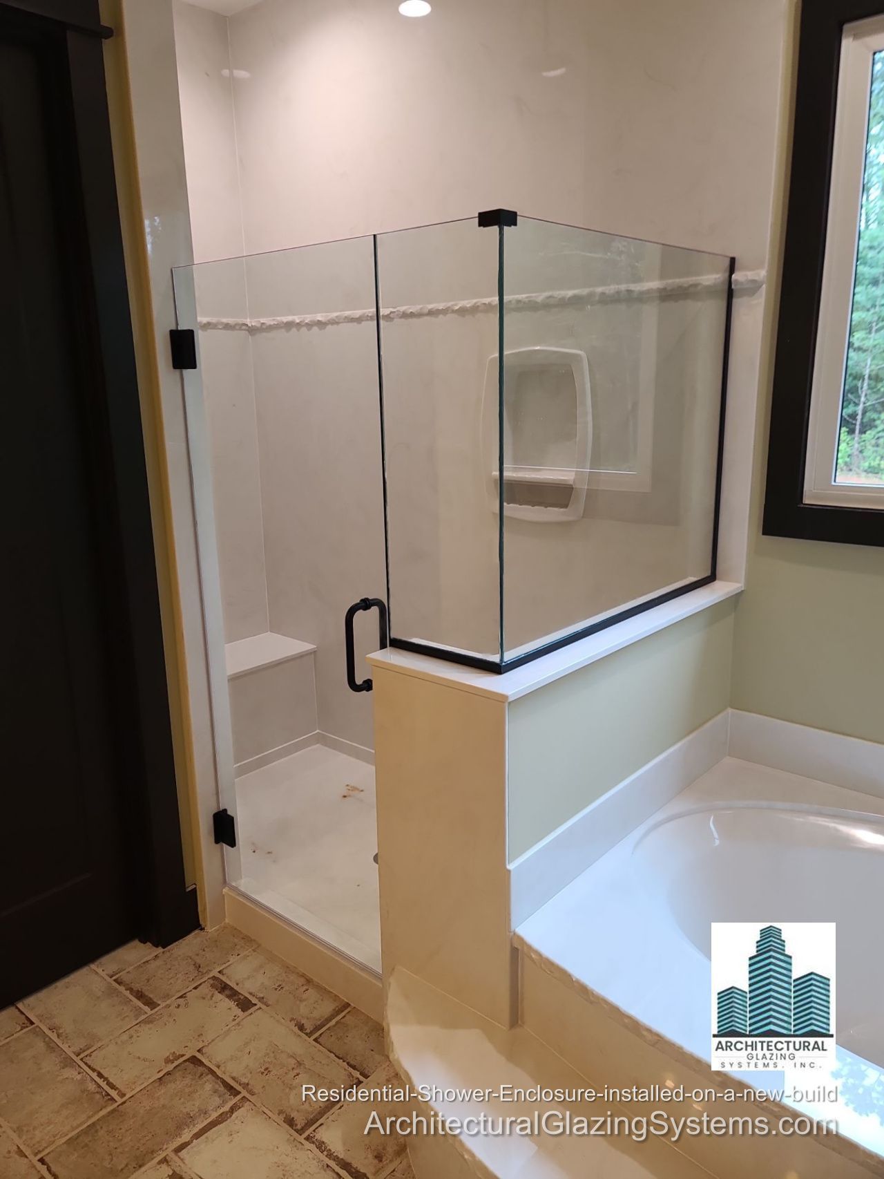 Clear-glass shower enclosure with a black handle and corner panel above a half wall beside a bathtub.