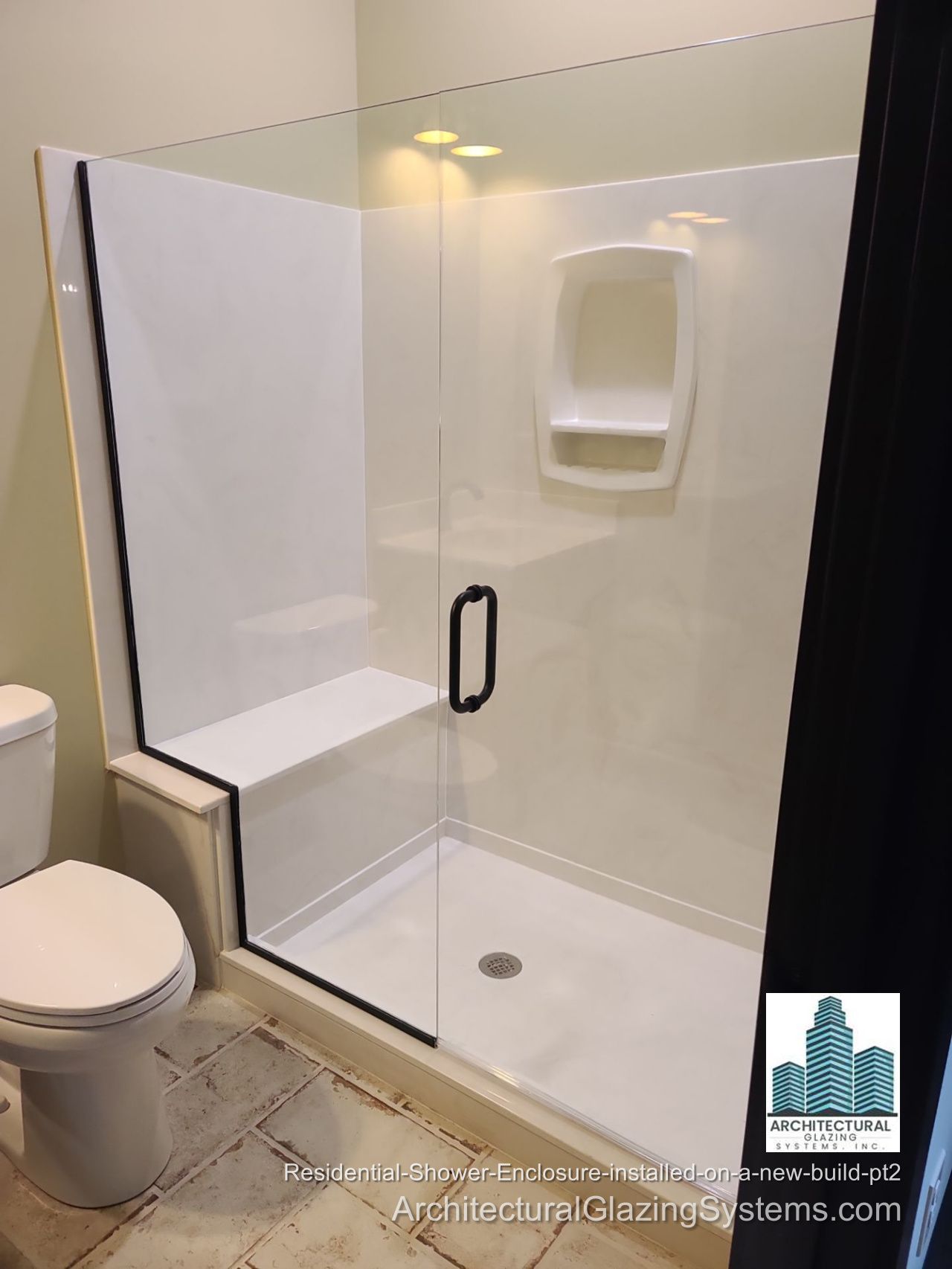 Clear-glass shower door with a black handle, a side panel above a half wall, and a built-in shower bench.