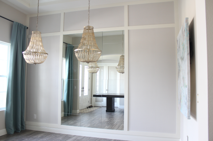 A room with a large mirror on the wall and two chandeliers hanging from the ceiling.
