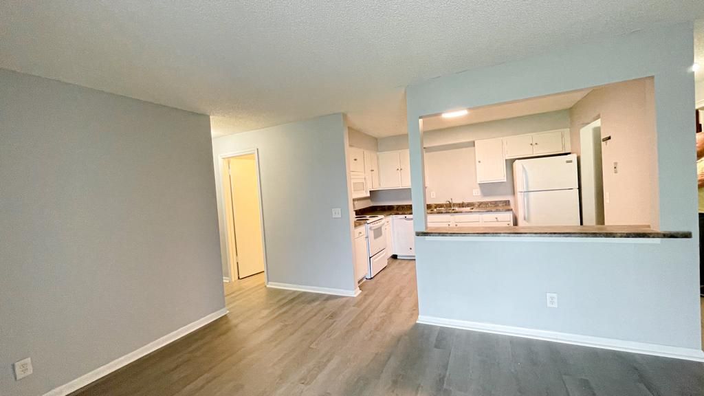 a living room with hardwood floors and a kitchen in the background .