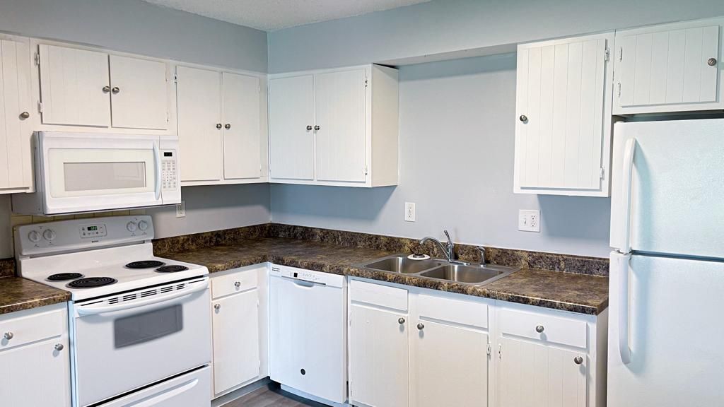 a kitchen with white cabinets , a stove , a refrigerator , a microwave , and a sink .