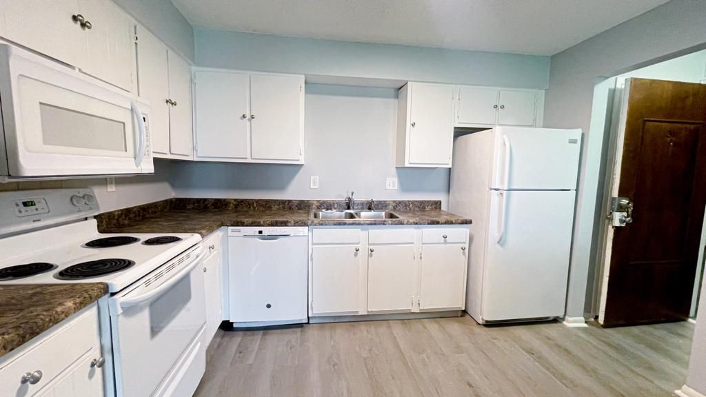 a kitchen with white cabinets , a stove , a refrigerator , and a microwave .