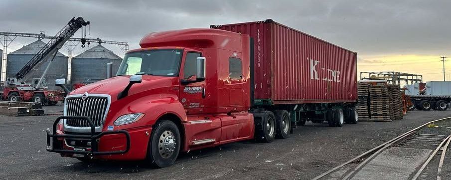 A red semi truck is parked next to a red shipping container.