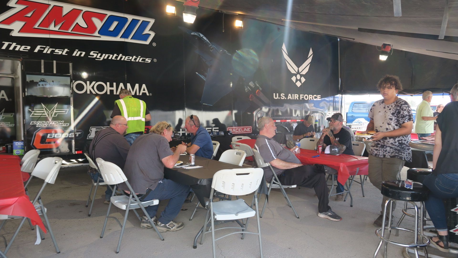 A group of people are sitting at tables in front of an amsoil truck.