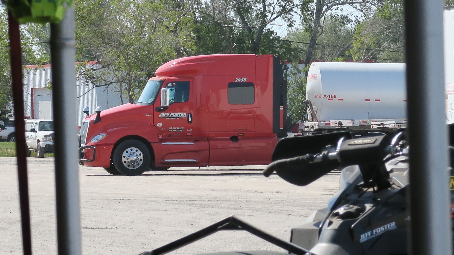 A red semi truck is parked in a parking lot next to a snowmobile.