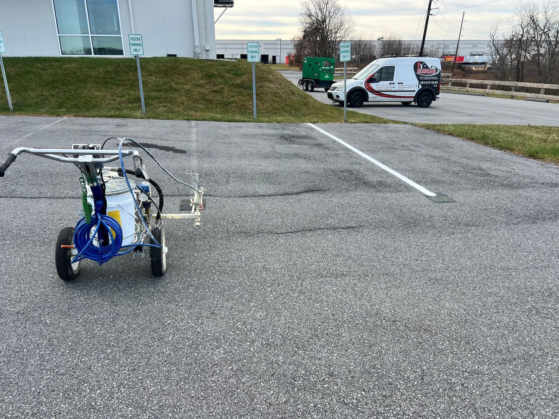 Line-painting machine in a parking lot, with a white van in the background, making a white parking stripe on asphalt.