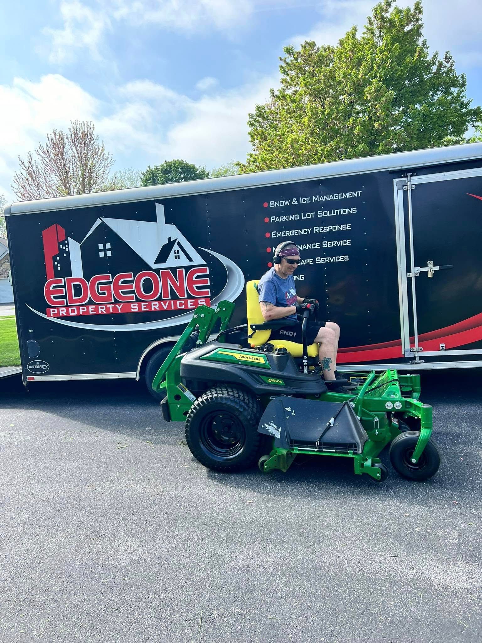 A person on a green lawnmower in front of a trailer with 