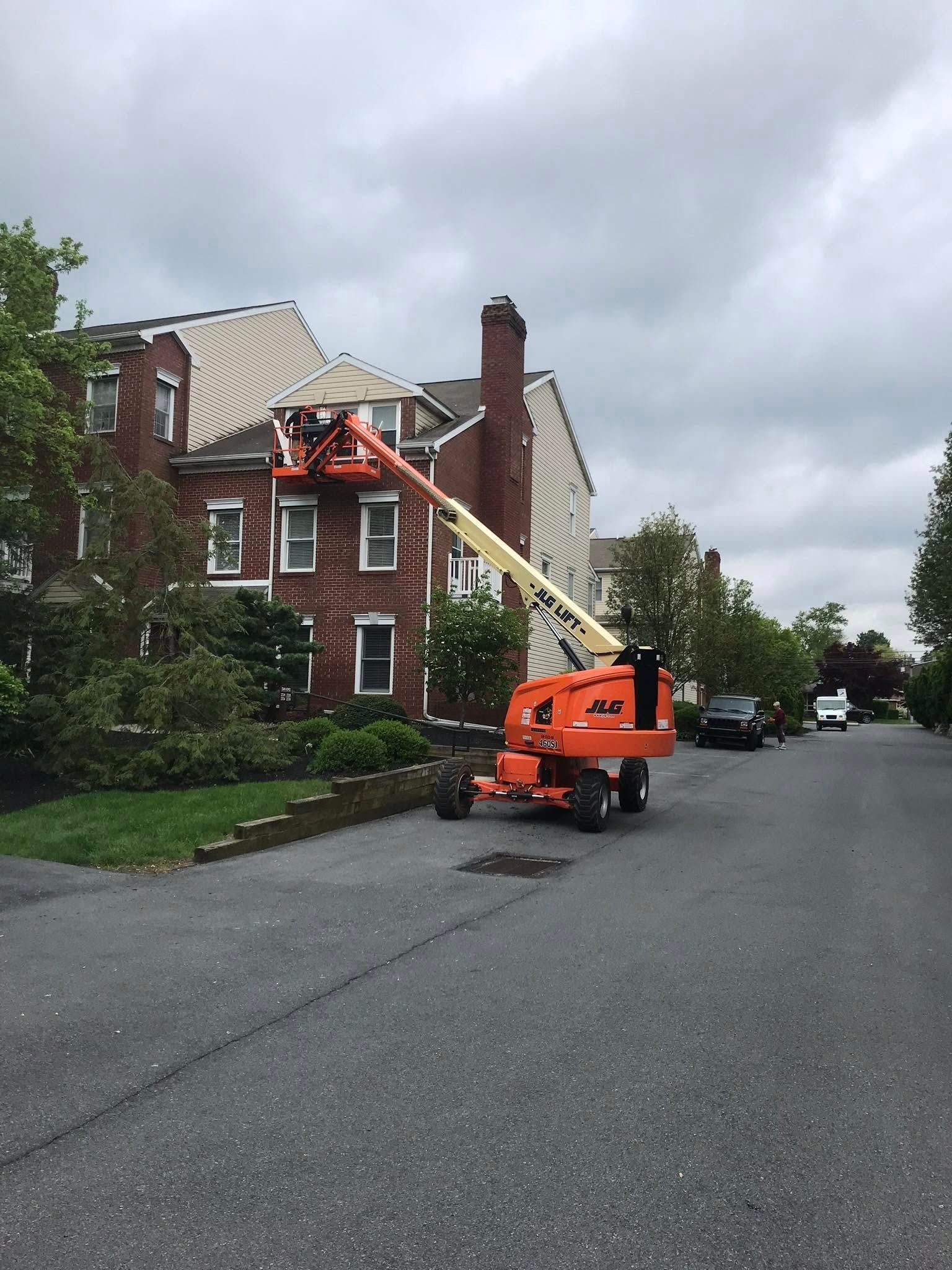 Orange lift crane next to a brick building on a street, cloudy sky.