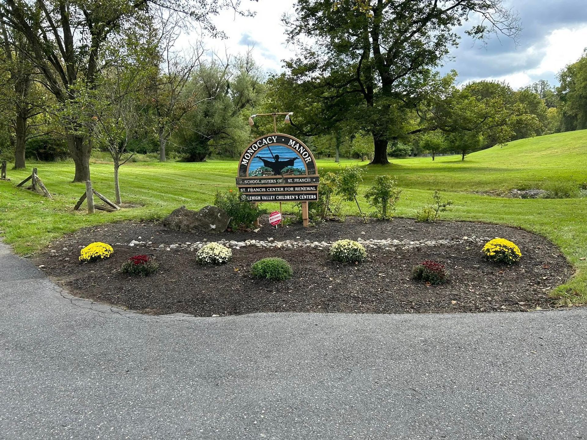 Bench with a sign in front of a flowerbed, set in a grassy park.