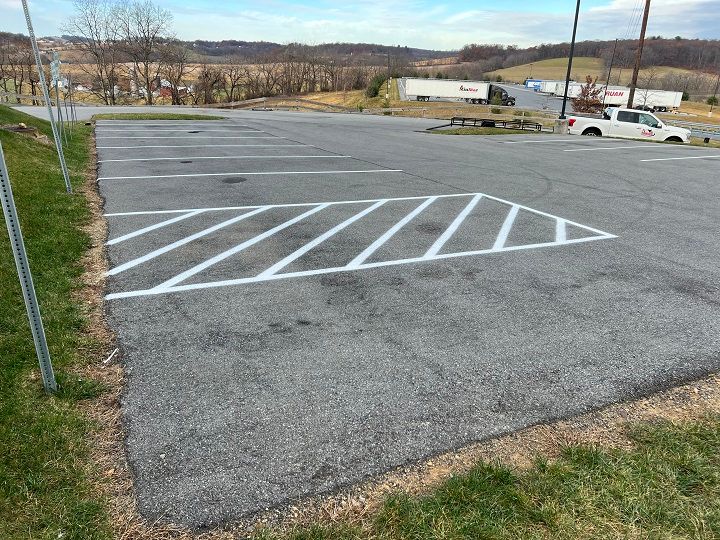 Empty asphalt parking lot with white diagonal parking space lines; grassy edge.