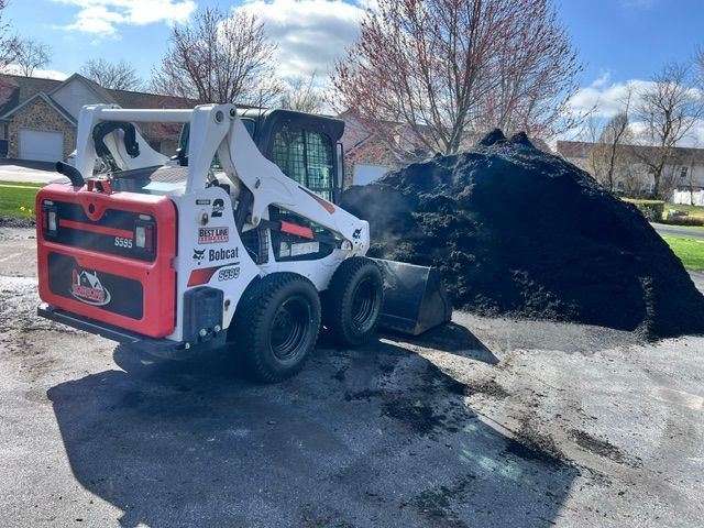Bobcat skid-steer loader next to a large pile of black mulch on a driveway.