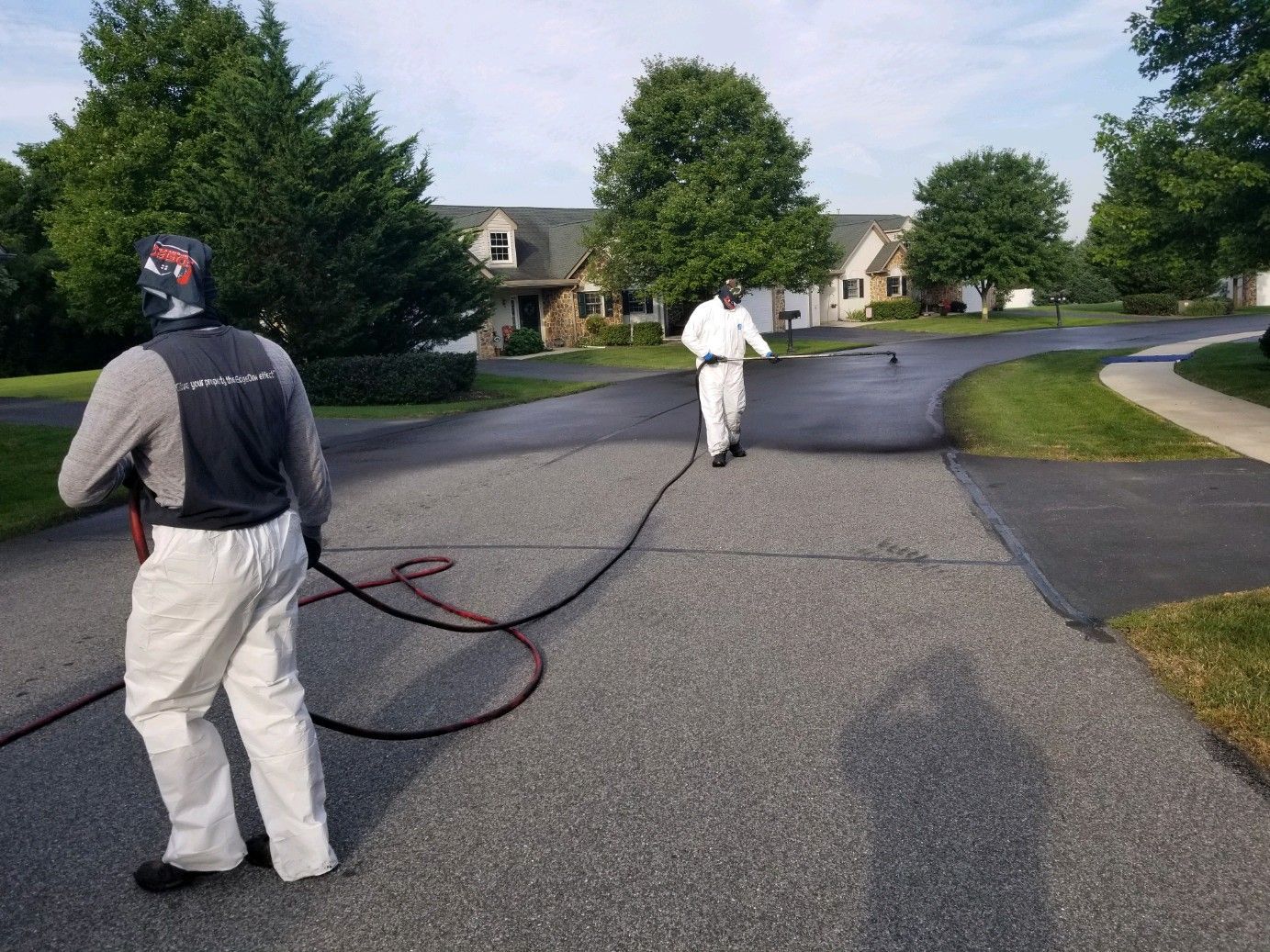 Two people in white protective suits applying sealant to a residential driveway.
