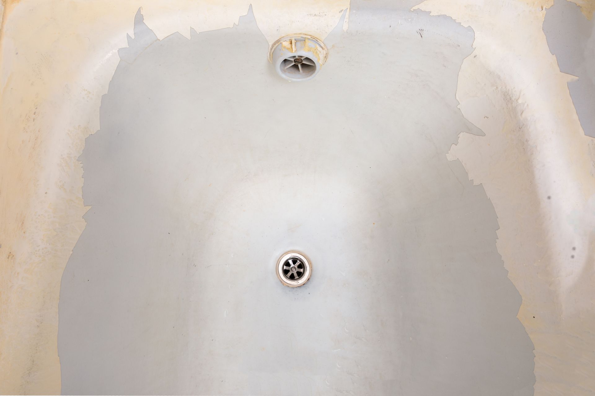 Empty bathtub with stained, patchy white surface and visible drain and overflow opening Empty bathtub with stained, patchy white surface and visible drain and overflow opening