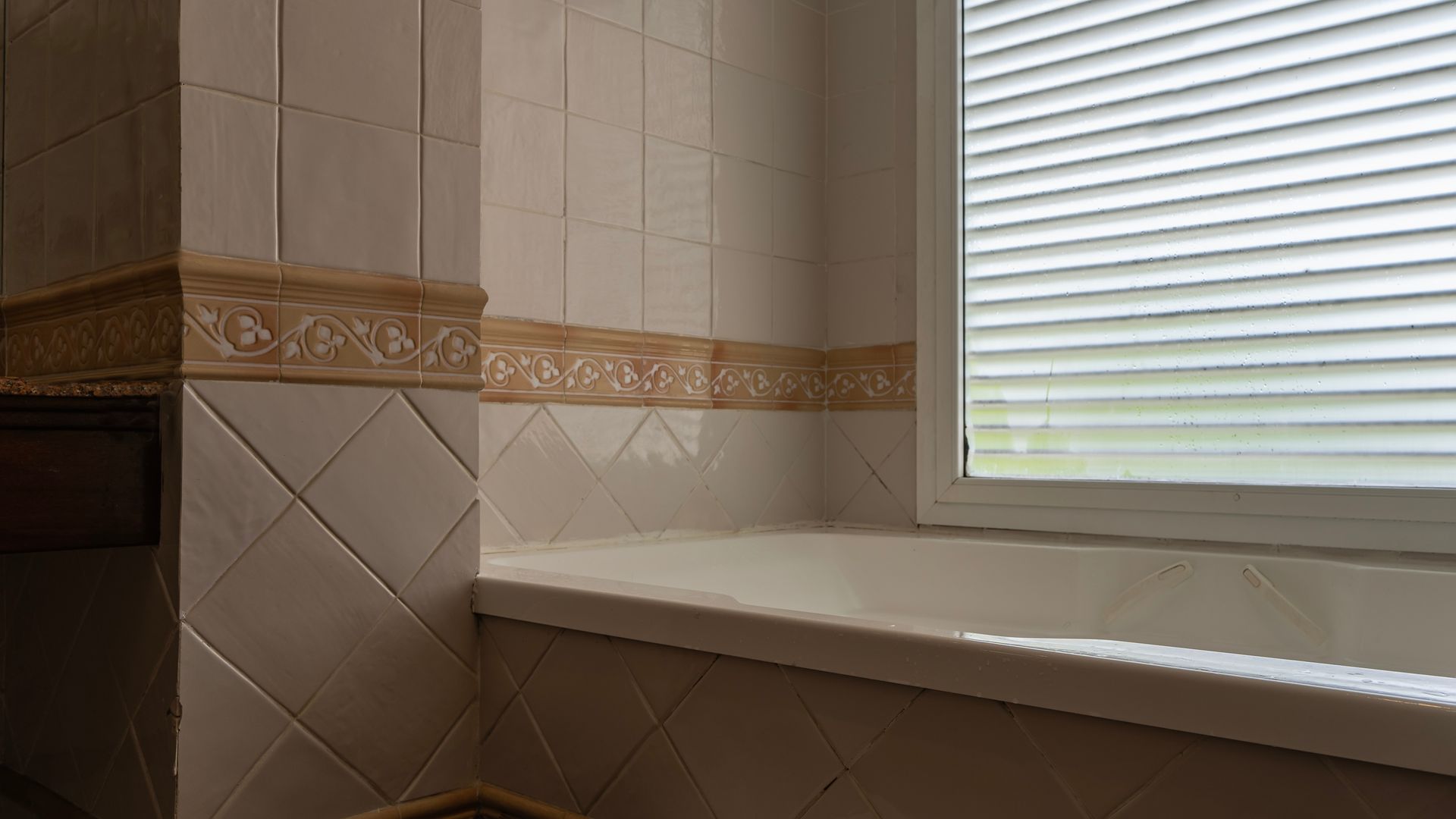 An older bathroom with a built-in tub, patterned tile border, and a window letting in natural light