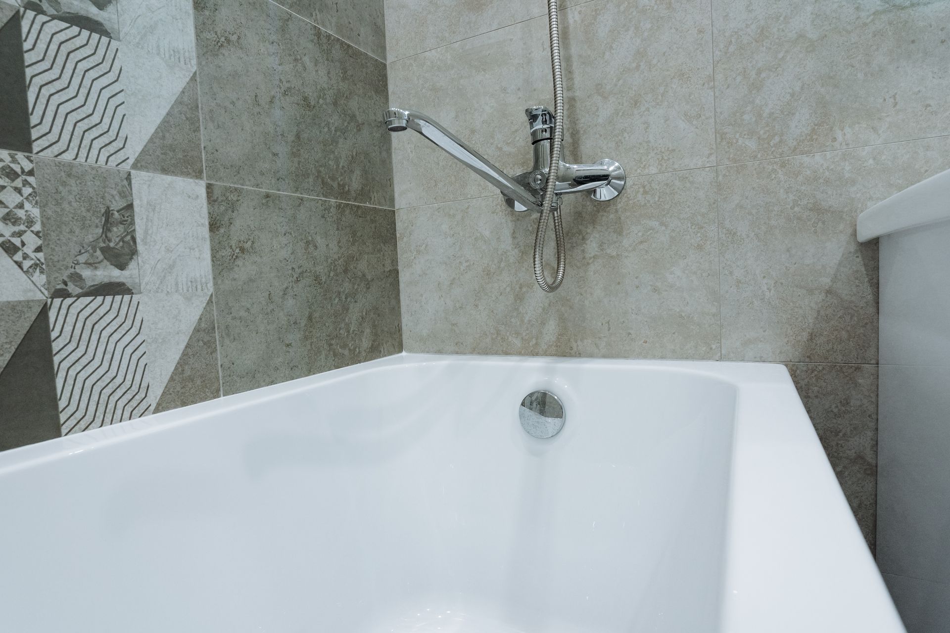 A white refinished bathtub with a chrome faucet and handheld showerhead against tiled bathroom walls