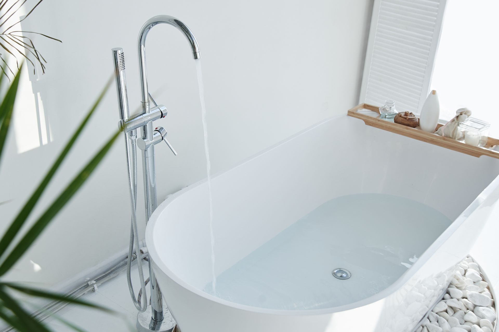 A modern freestanding bathtub filling with water from a sleek chrome faucet in a minimalist bathroom