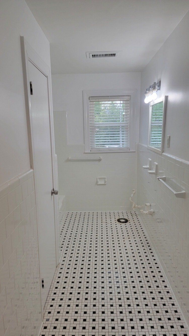 White bathroom with a walk-in shower, window blinds, and patterned tile floor.