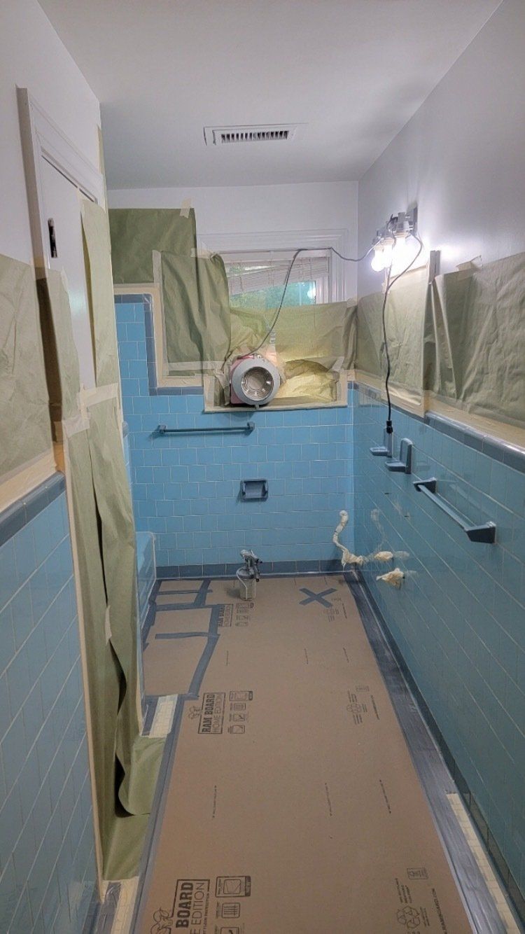 Narrow hallway under renovation, with blue lower walls, covered windows, and floor protected by cardboard and plastic.