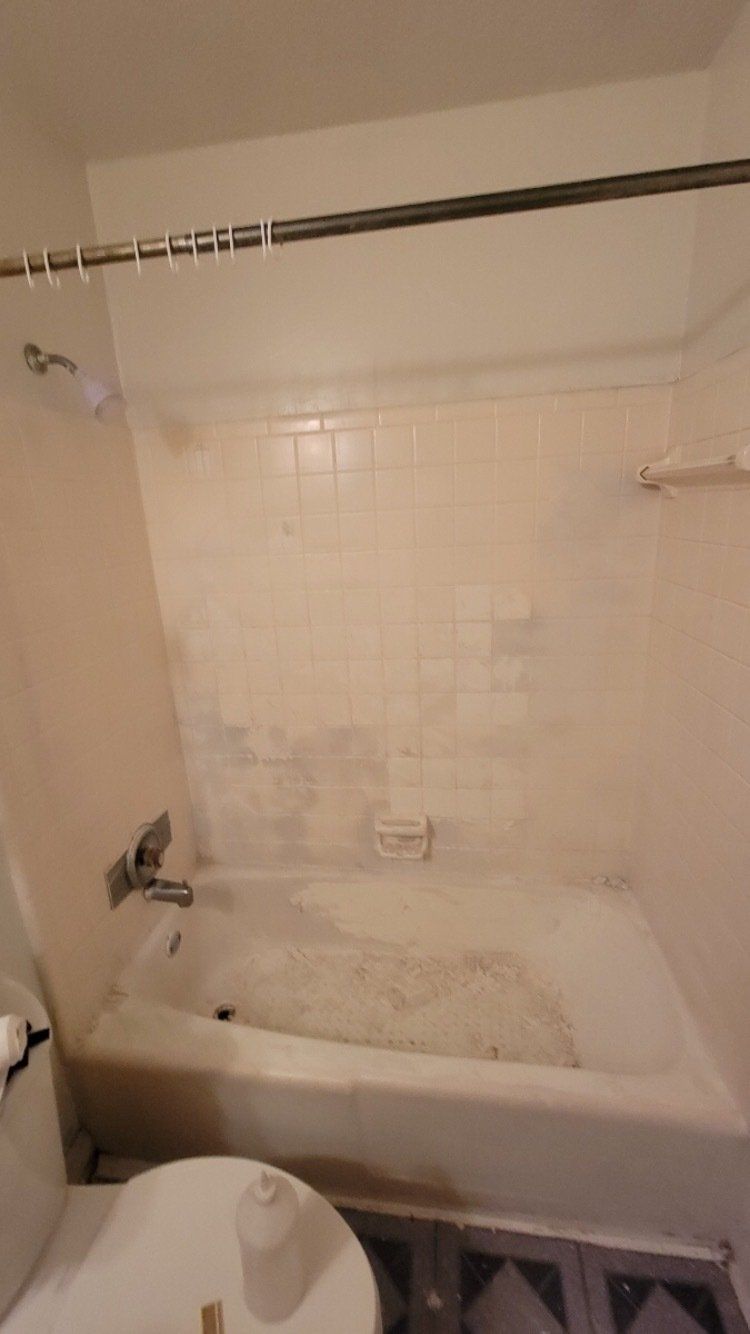 A worn bathtub and shower surround with stained off-white tile and a curtain rod above.