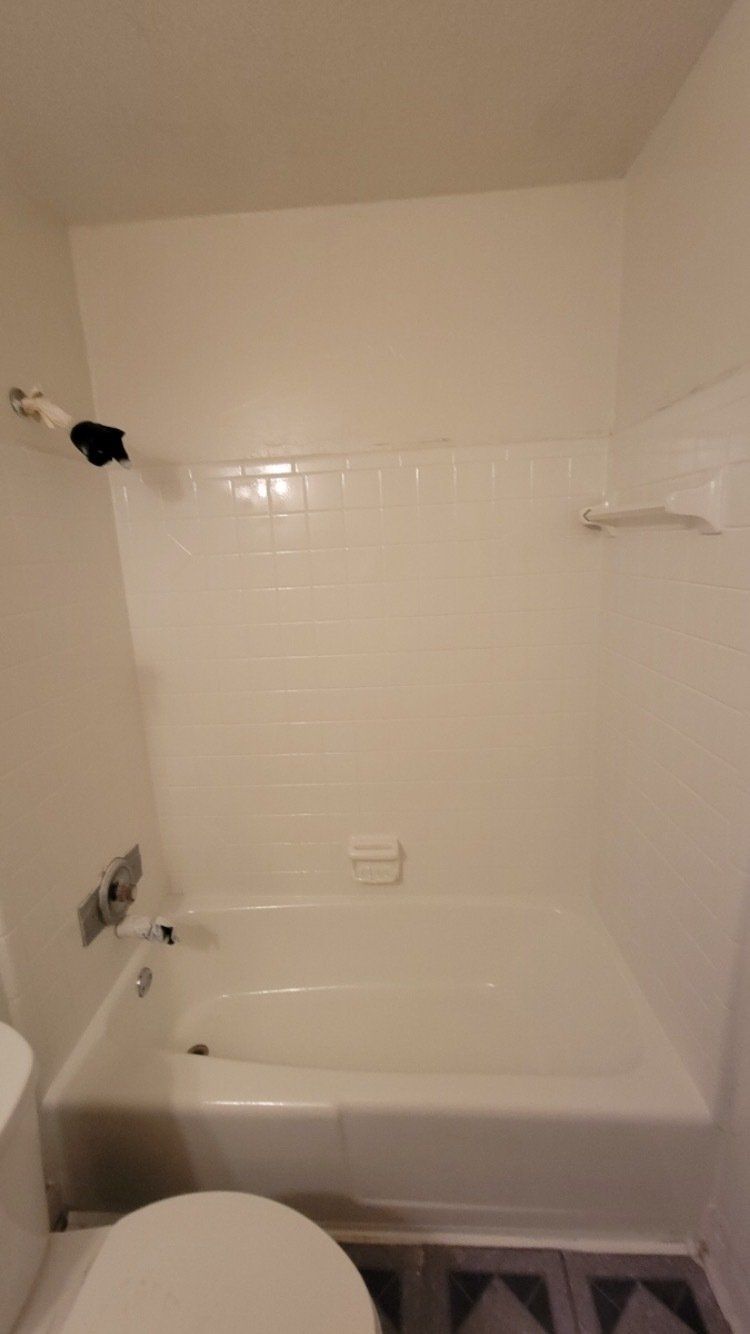 Small white bathroom with a tub-shower, tiled walls, and a towel rack.