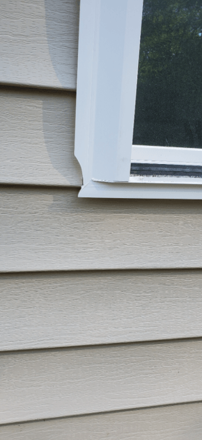 Close-up of beige house siding and a white window frame with dark glass