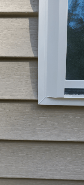White house siding beside a white-trimmed window with dark glass and a visible sill