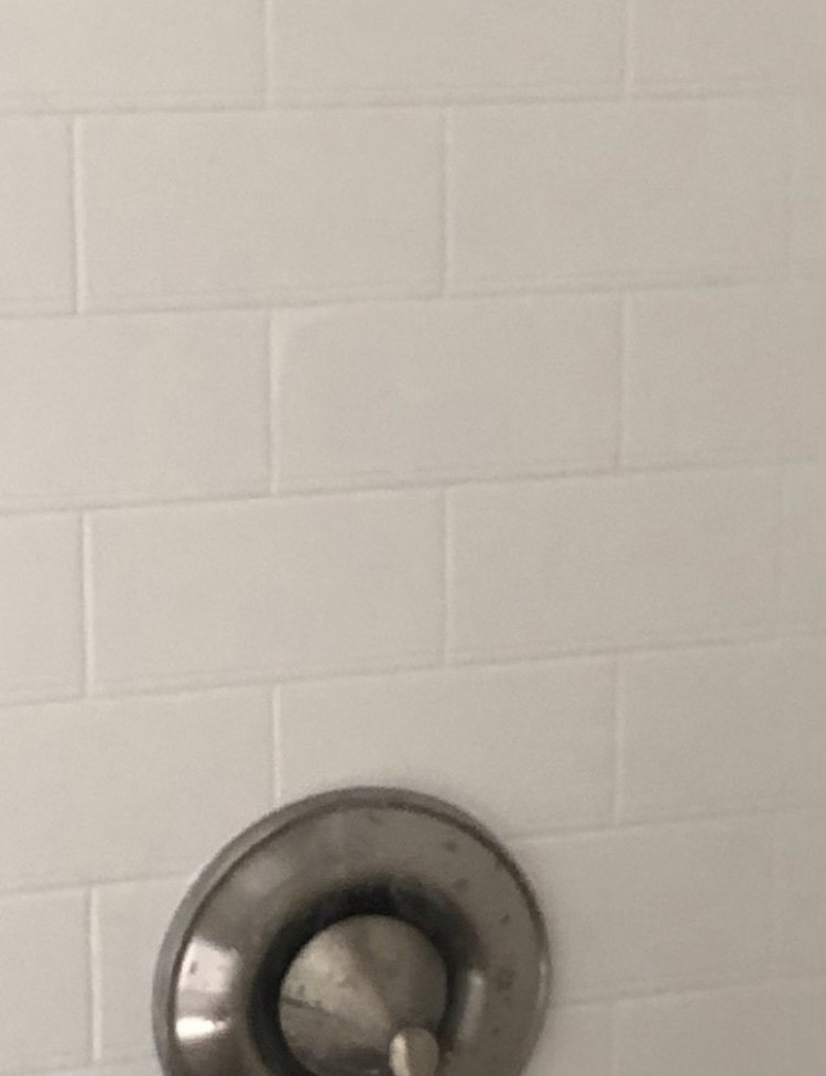 Silver wall-mounted bathroom flush valve on a white tiled wall
