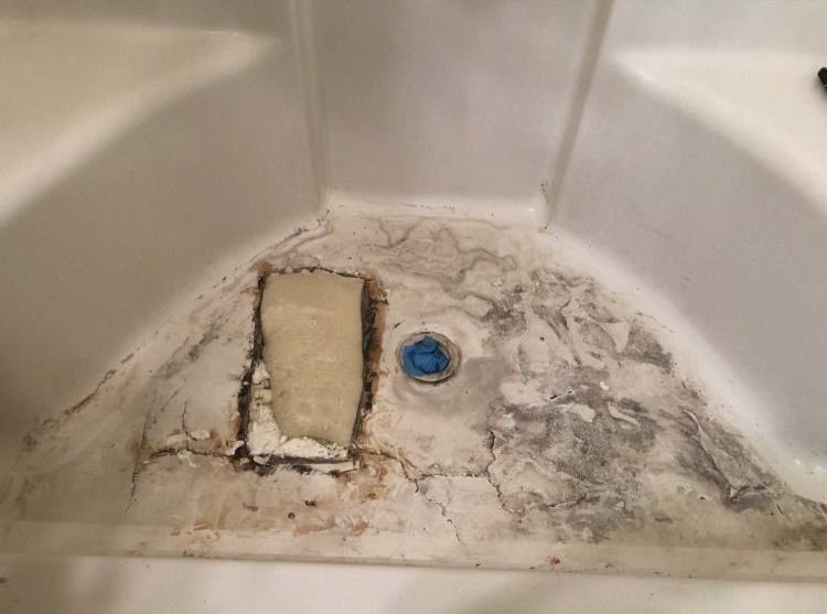 Moldy, stained bathtub corner with a broken soap dish and blue drain plug