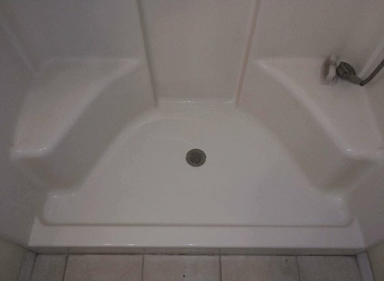 Empty white shower stall with a center drain and tiled floor edge