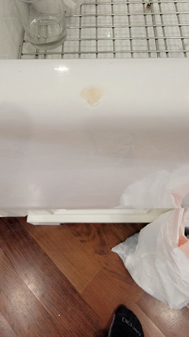 White appliance with a small stain, on a tiled floor beside a plastic bag and a shoe.