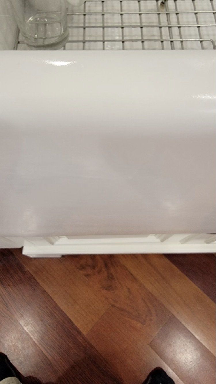 White appliance or cabinet on a wooden floor, with a wire rack visible behind it.