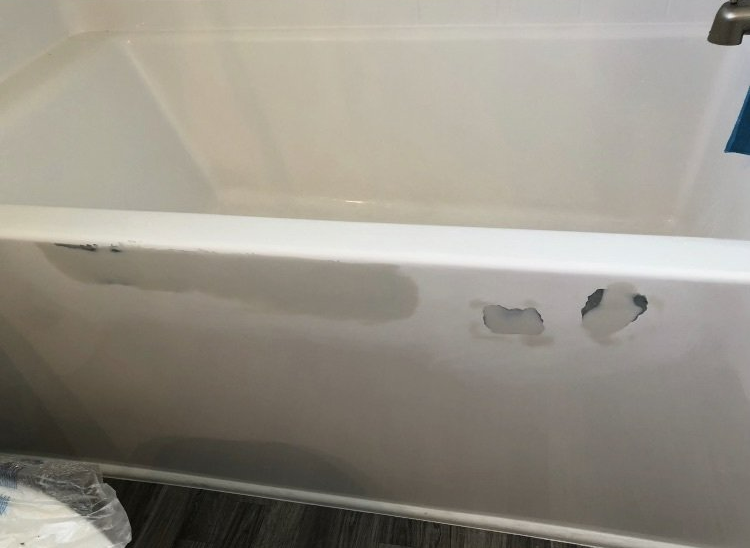 White bathtub with chipped and peeling paint along the side wall.