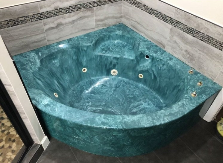 Teal corner jacuzzi tub with multiple jets in a tiled bathroom
