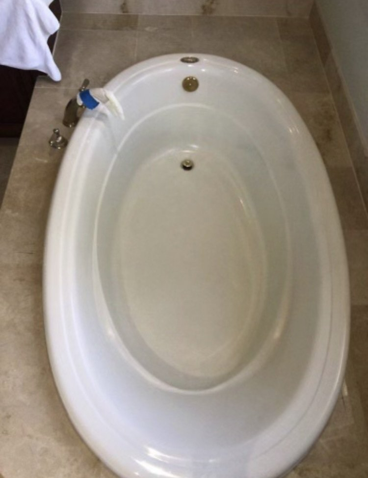 White oval bathtub viewed from above on a beige tiled floor, with a faucet and drain visible.