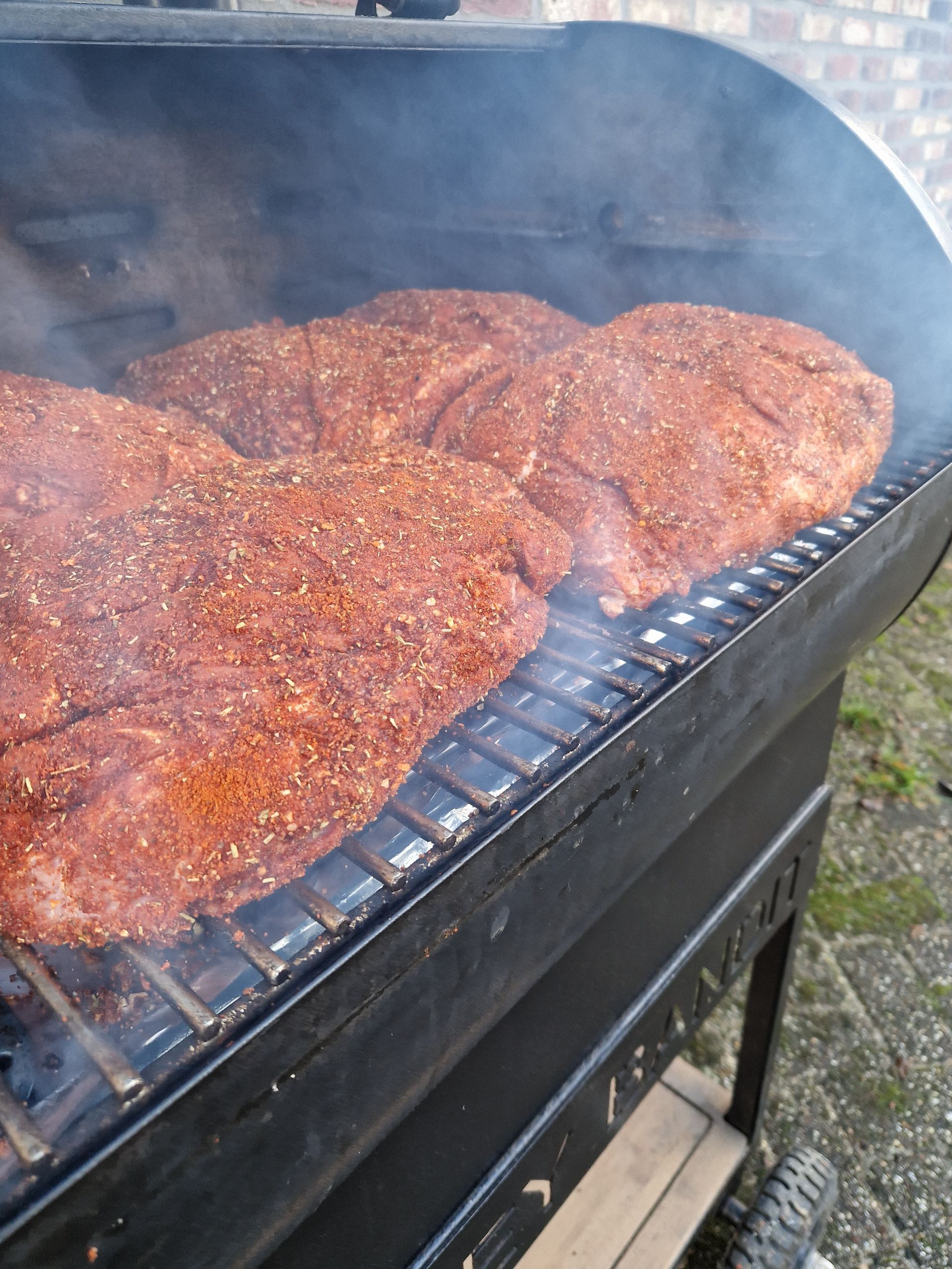 Drie gekruide stukken vlees worden gerookt op een zwarte houtskoolgrill.
