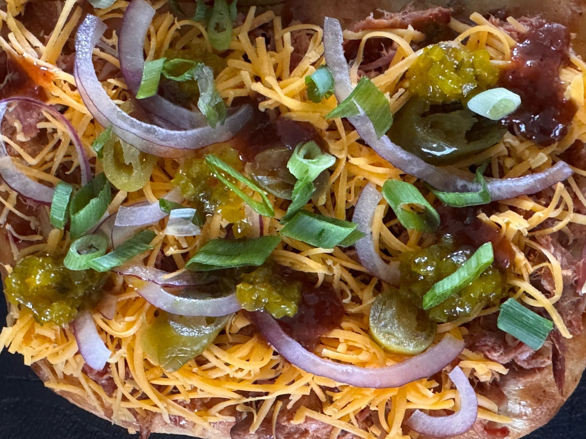 Een platbrood belegd met geraspte kaas, dun gesneden rode ui, blokjes groene paprika en stukjes vlees.