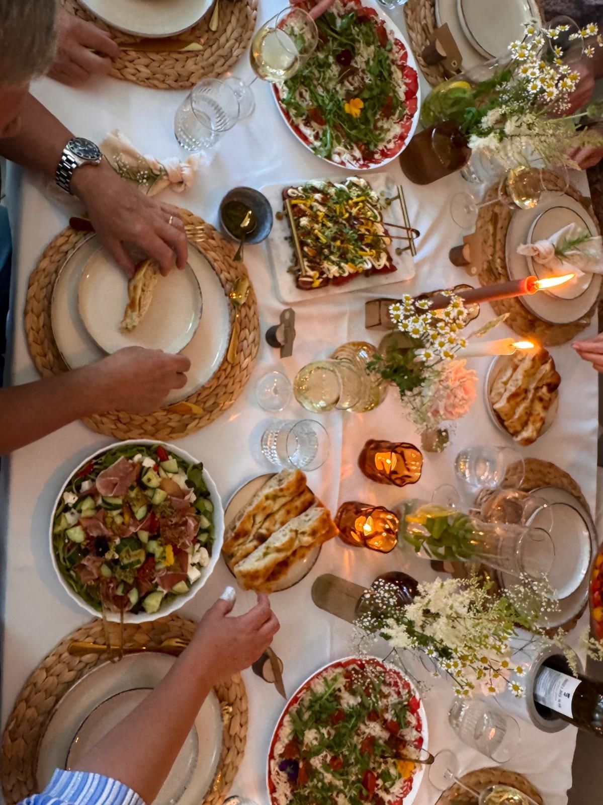 De tafel is gedekt voor een diner met borden, wijnglazen en een grote schaal salade met rucola en bessen.