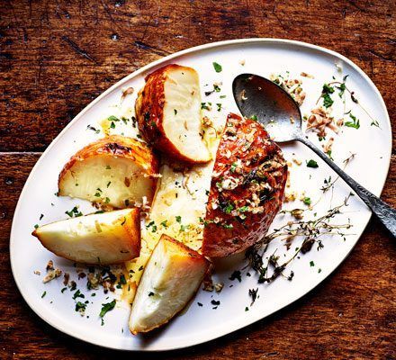 Geroosterde aardappelpartjes, gekruid met specerijen, op een witte serveerschaal met een metalen lepel, op een rustieke houten tafel.