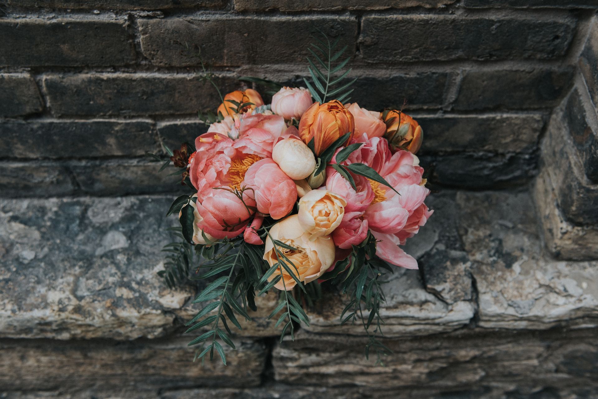 Bouquet of pink and peach flowers resting on a stone step against a dark brick wall