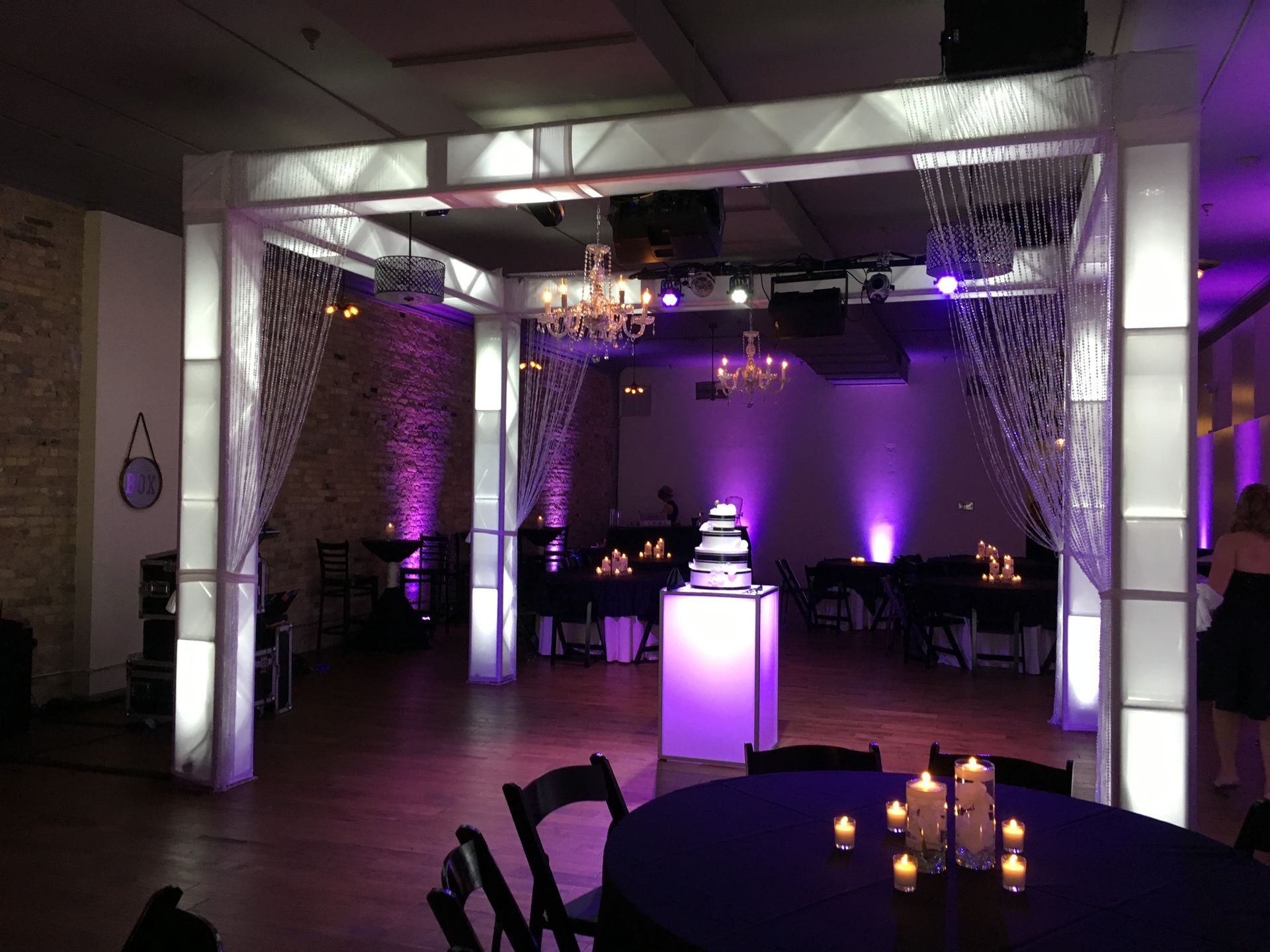 Purple-lit event venue with tables, chairs, and a glowing central display near the back wall