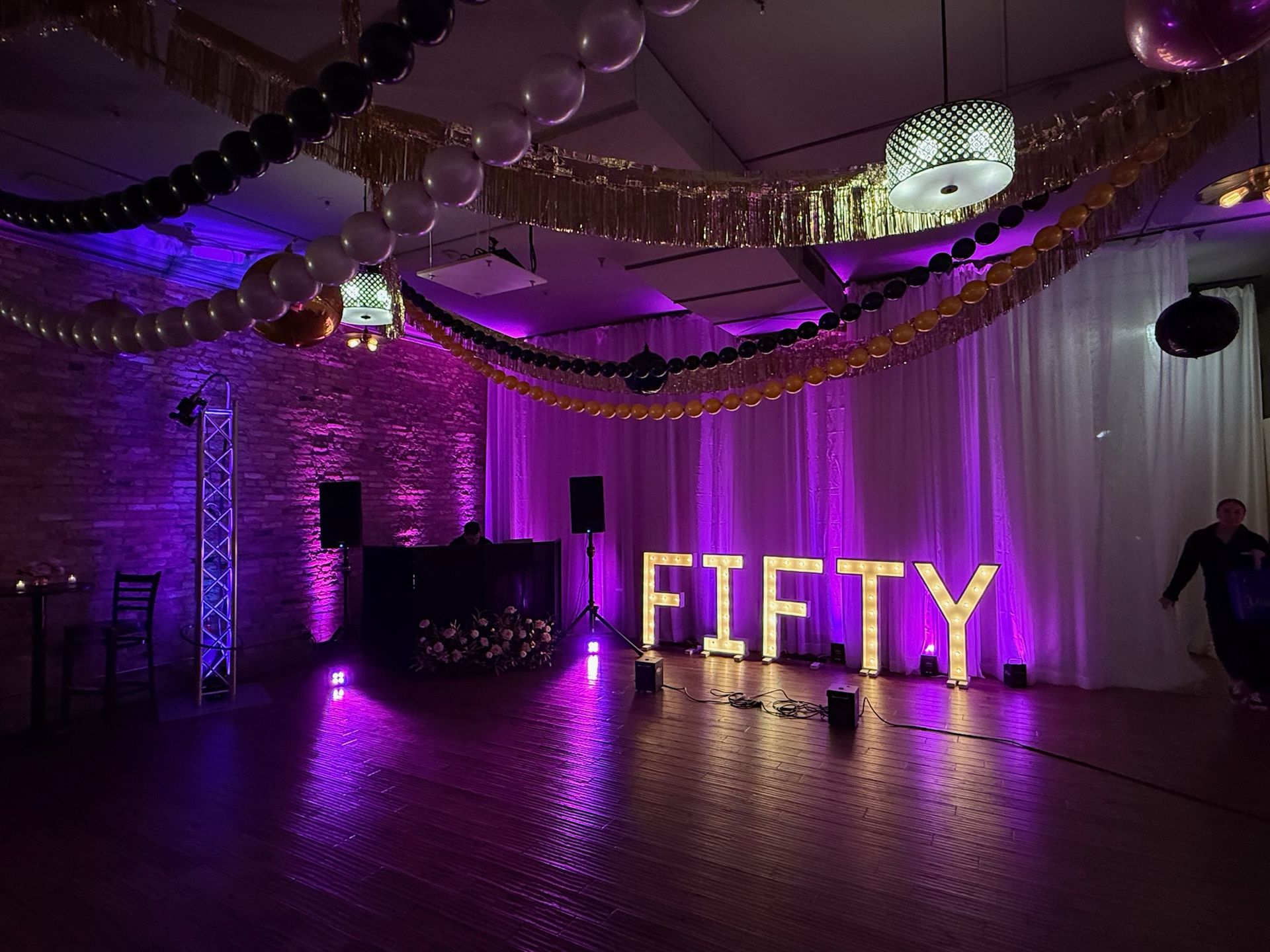 Purple-lit banquet hall with hanging decorations and large illuminated “FIFTY” letters on the floor