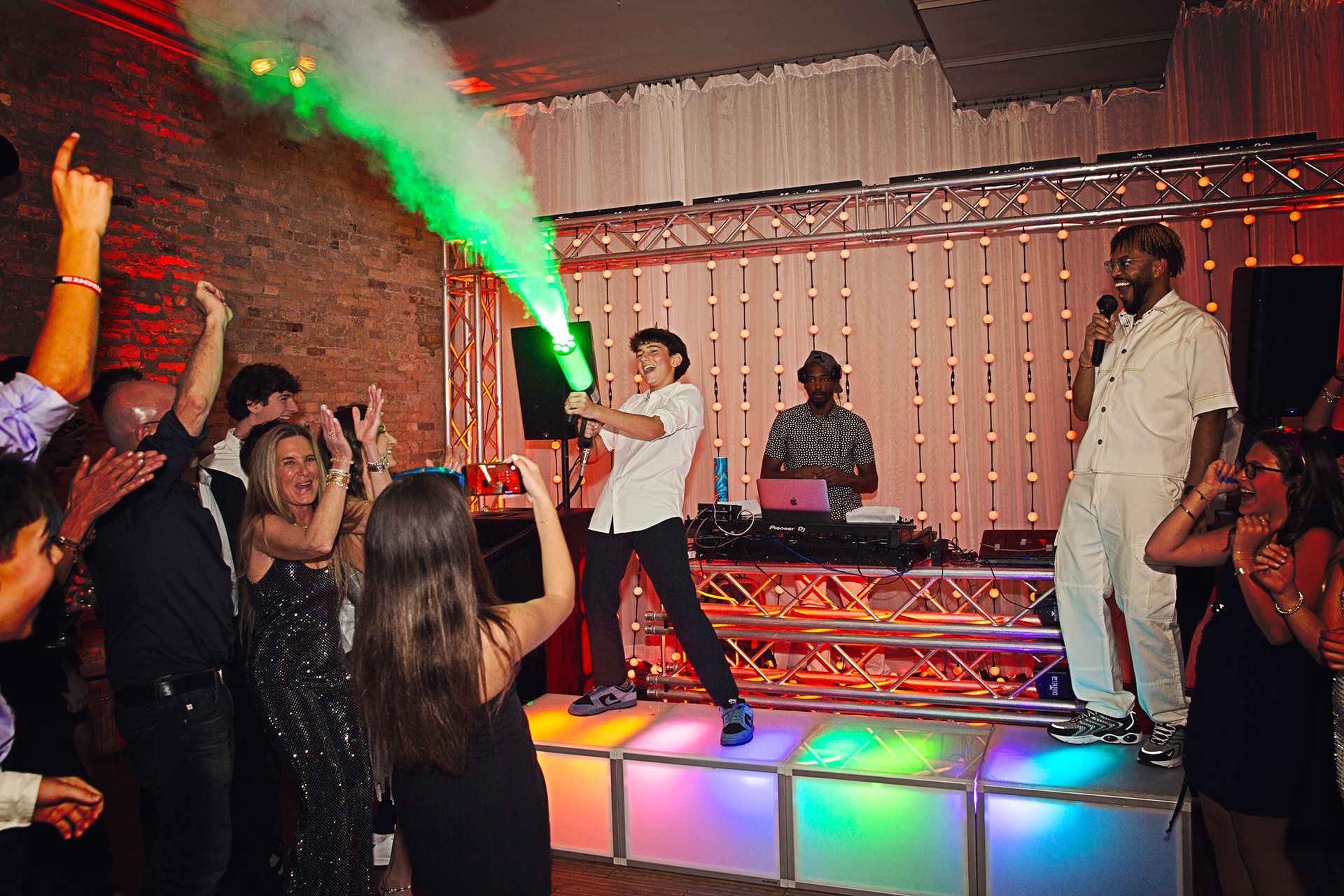 Person performing on a lit stage while a crowd dances at a party with green light effects.