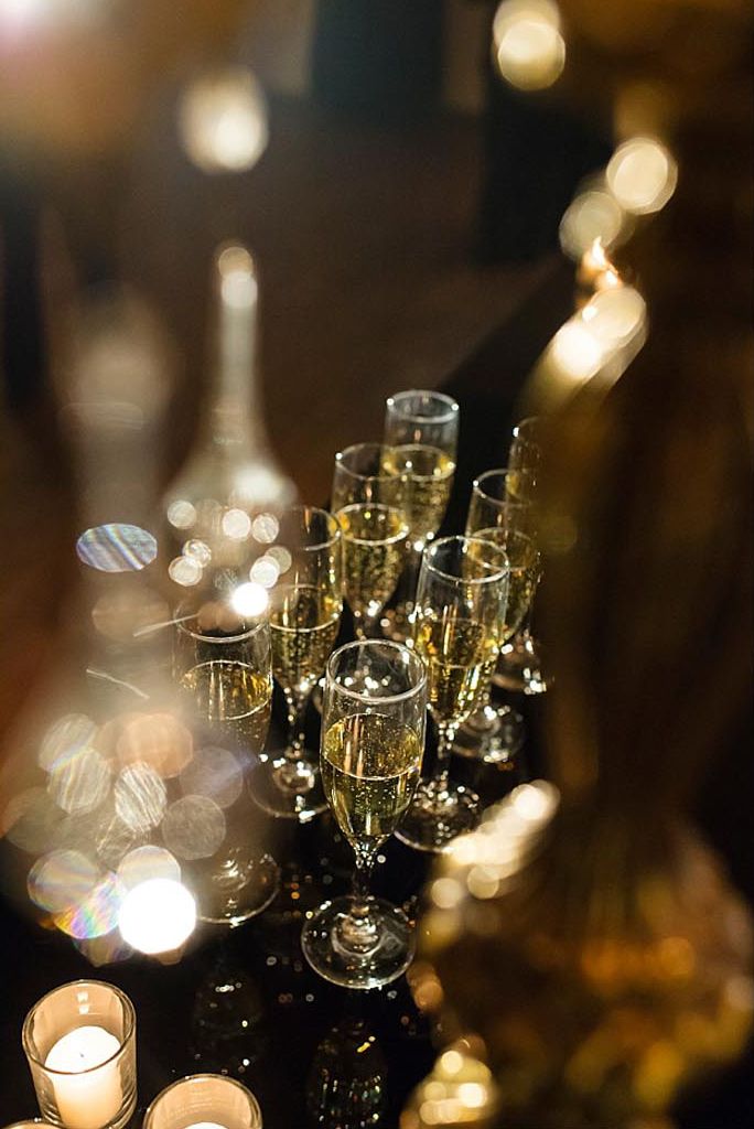 Rows of champagne flutes on a glowing tray, lit by warm bokeh lights in a dim setting