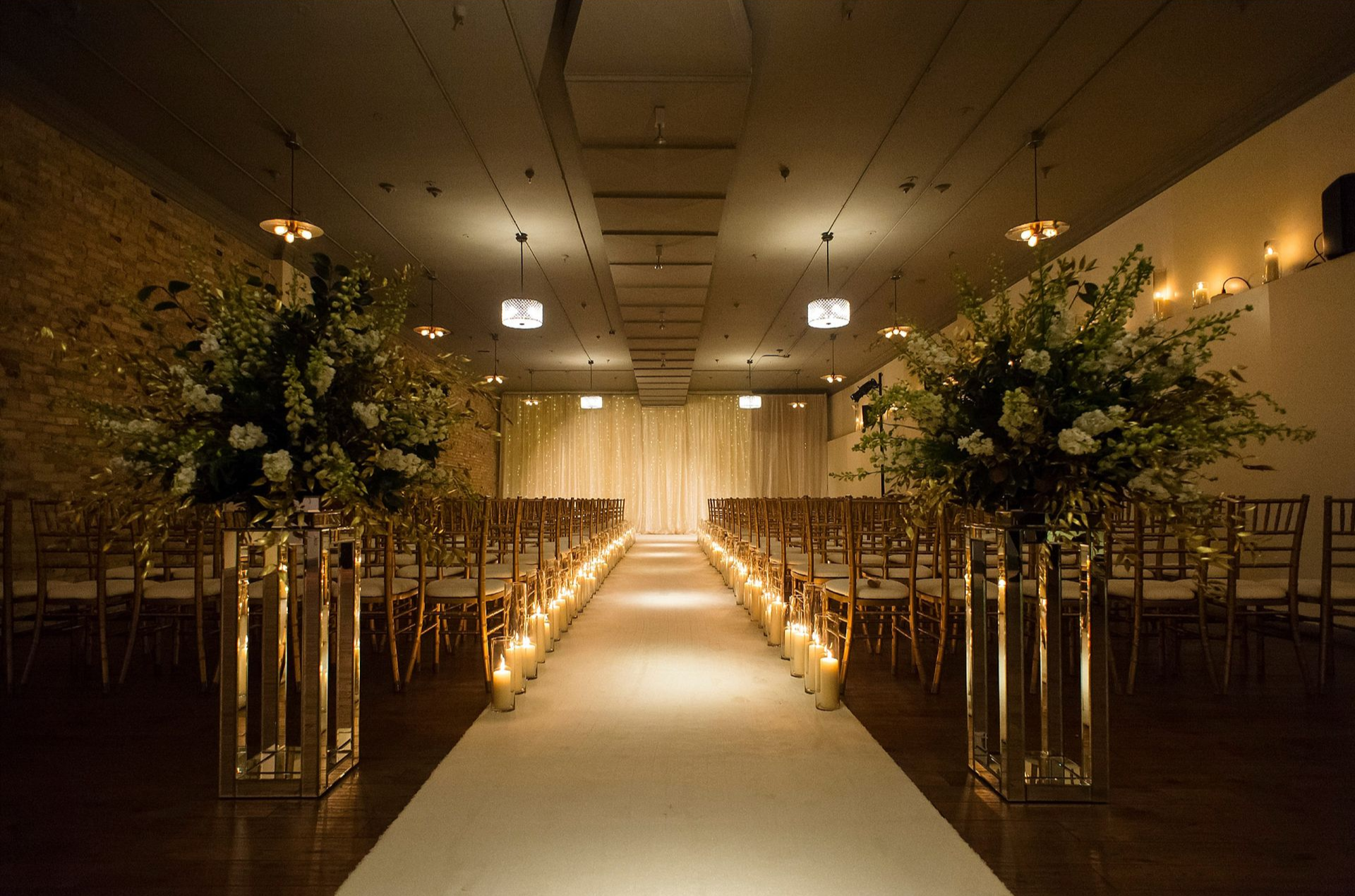 Elegant indoor wedding aisle with floral arrangements and rows of chairs leading to a curtained altar