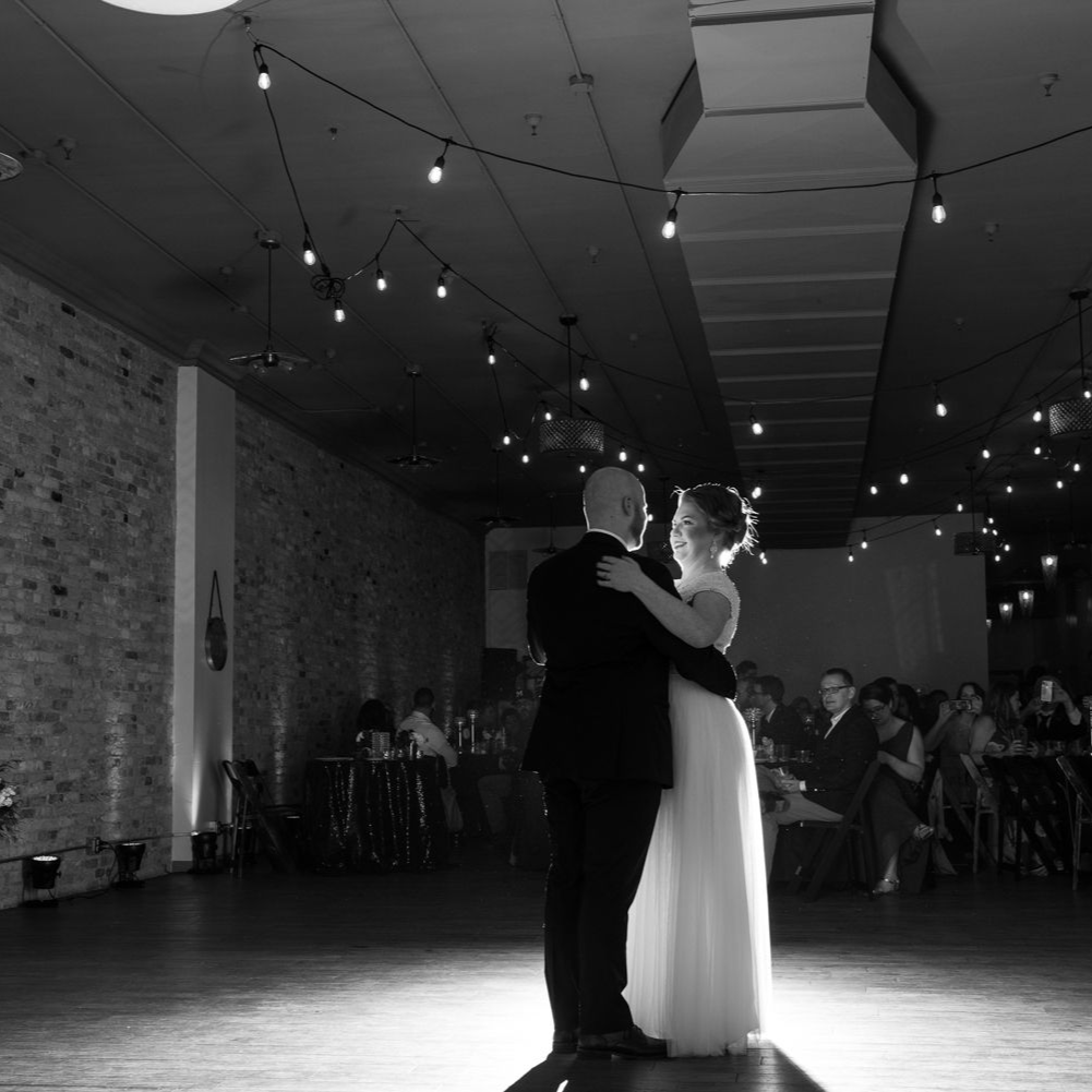 Bride and groom dancing in a decorated ballroom with guests watching