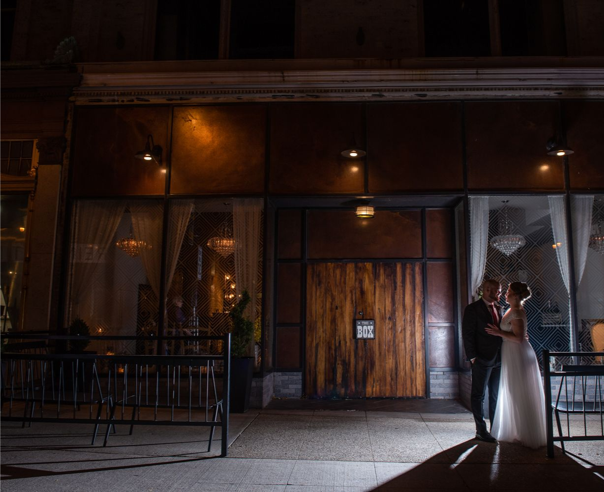 Bride and groom standing under lights outside a building at night