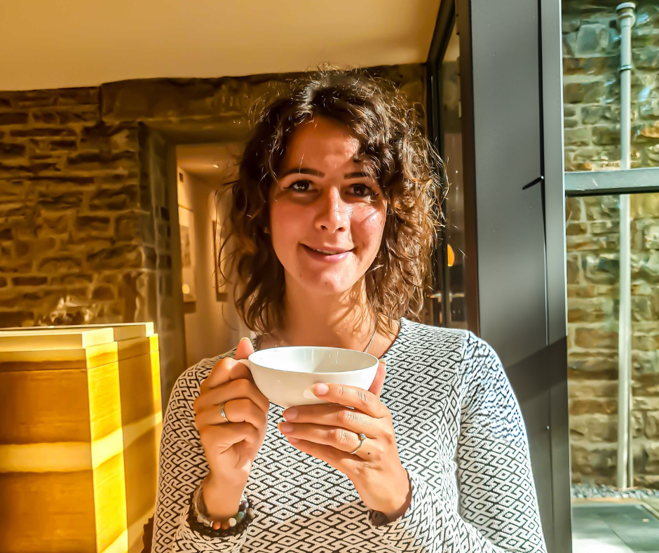 Eine braunhaarige Frau hält lächelnd eine Teetasse in den Händen.
