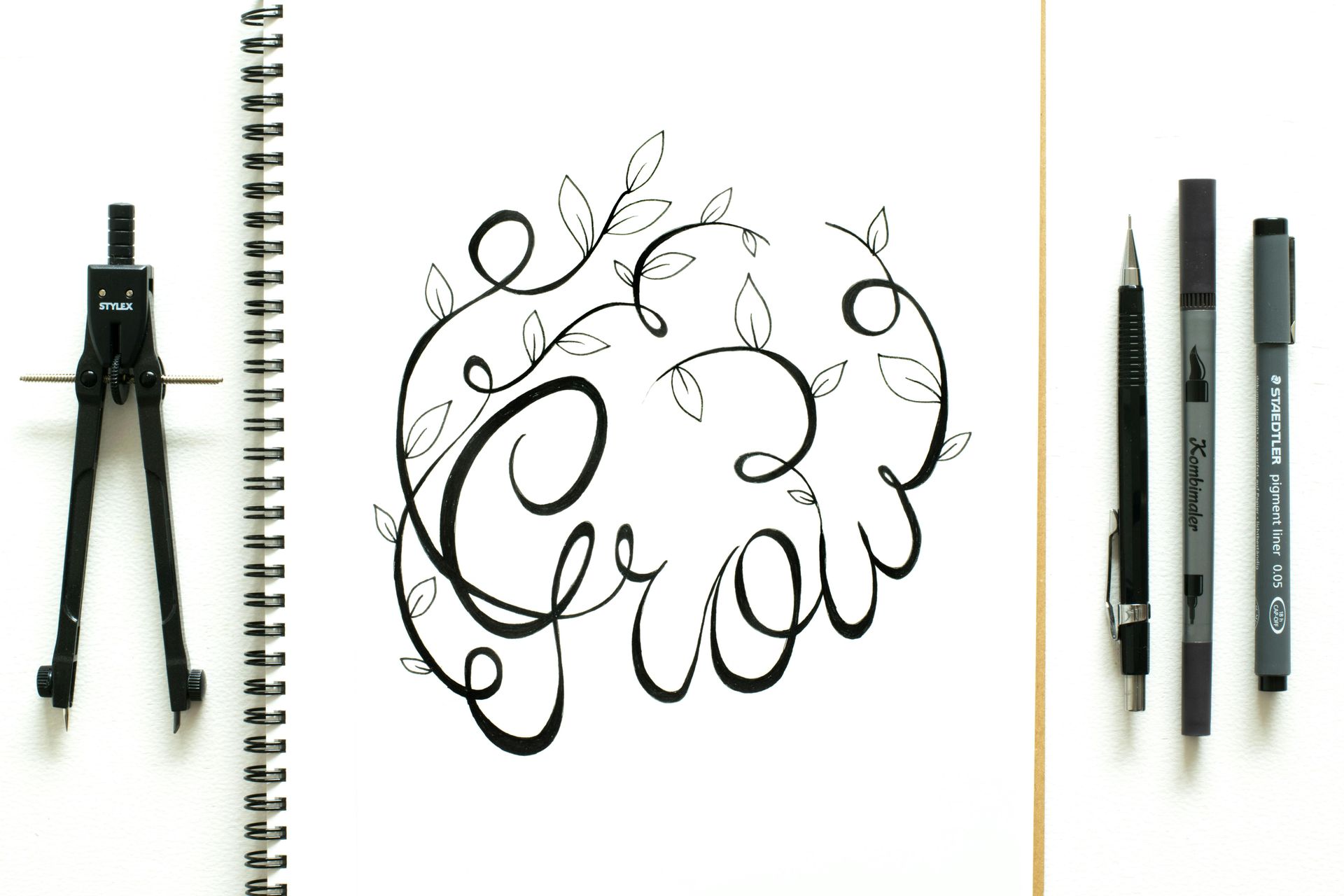 Zirkel, Stifte und das Wort „Grow“ in Kalligrafie – kreative Planung und Wachstum mit Vision Board.
