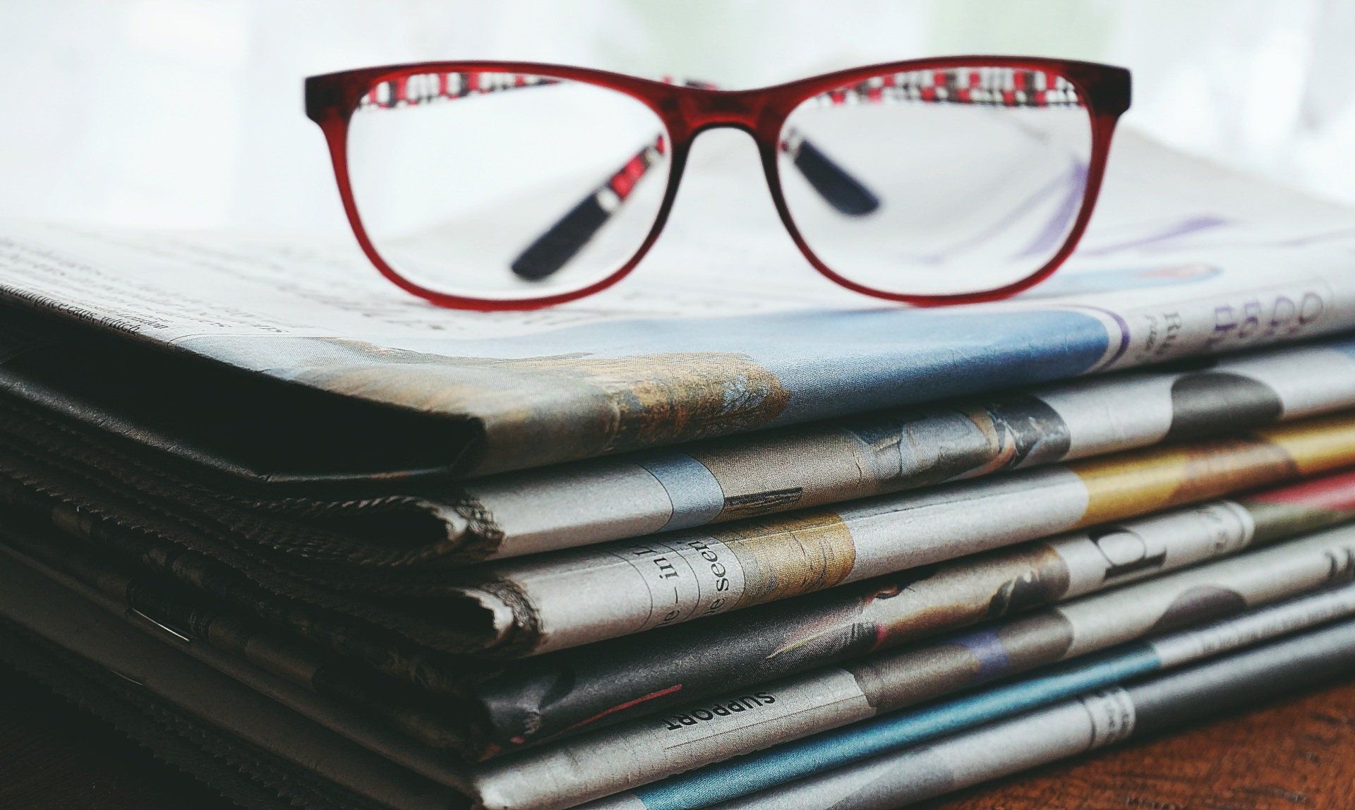 Rote Brille auf Zeitungen – Sinnbild für scharfen Blick, Klarheit und journalistische Achtsamkeit.