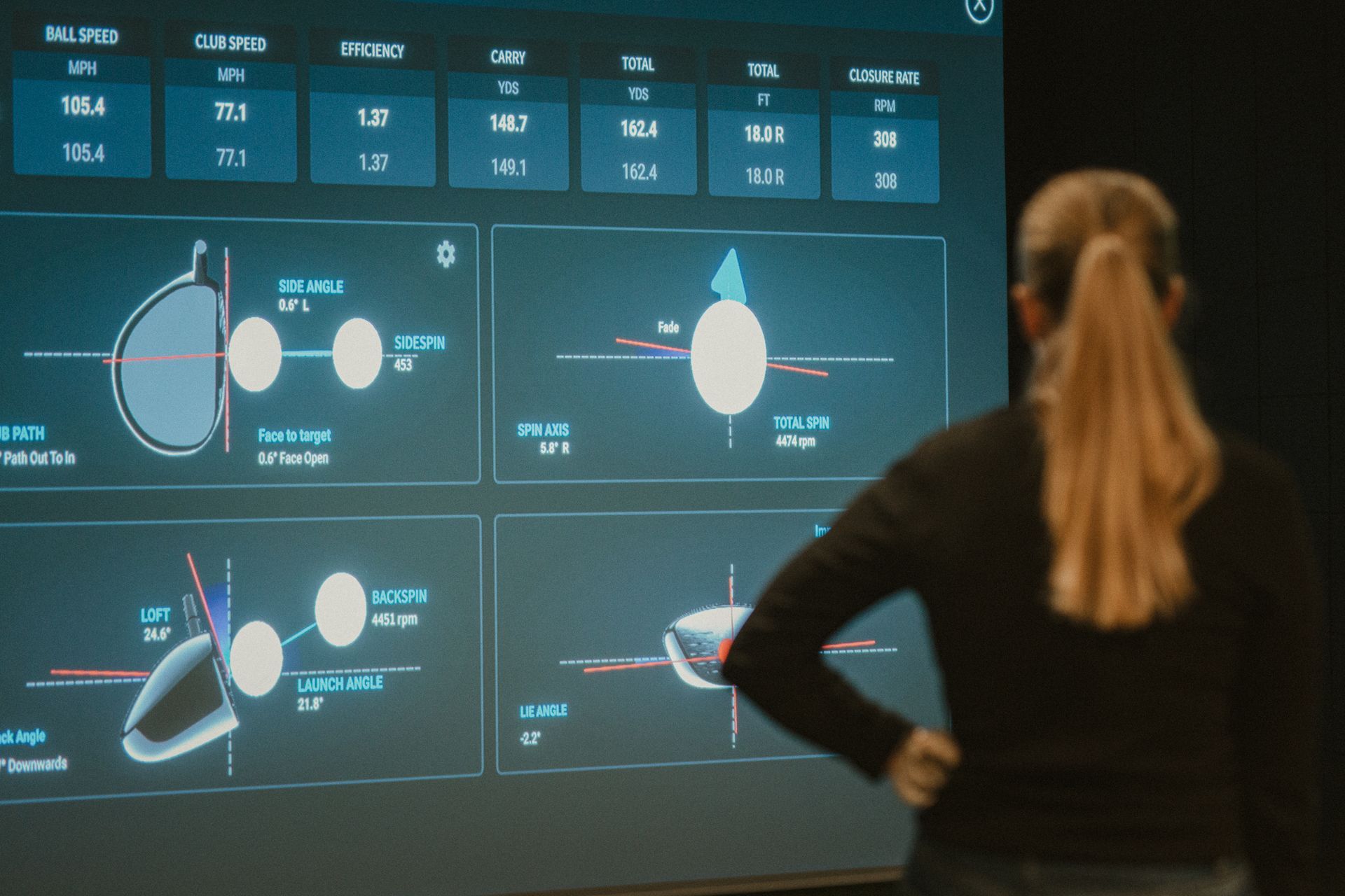 Woman analyzing golf swing data on a screen showing ball speed, club speed, and shot trajectory.